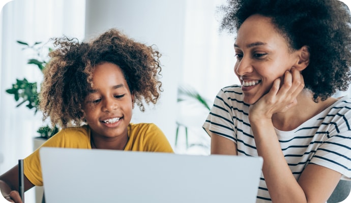 A yong girl with her mother smiling looking at a Laptop.